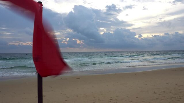 A red flag is a ban on swimming in this place. Yellow sand of the beach, sunset with big blue clouds. Waves in the sea. The guy is engaged in kitesurfing. Translation: Don't swim in this area