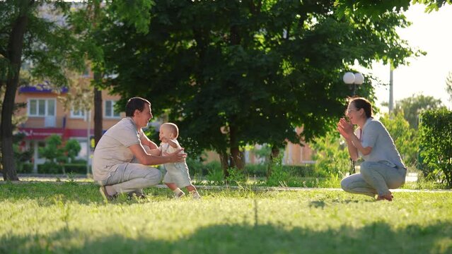 baby first steps parents. the kid took his first steps in the park next to his parents family. baby happiness on the faces of adults. waiting for the first step lifestyle from the child