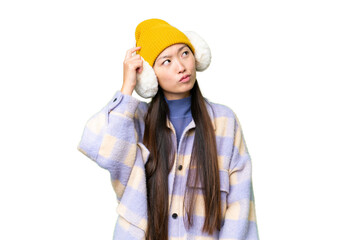 Young Asian woman wearing winter muffs over isolated chroma key background having doubts and with confuse face expression