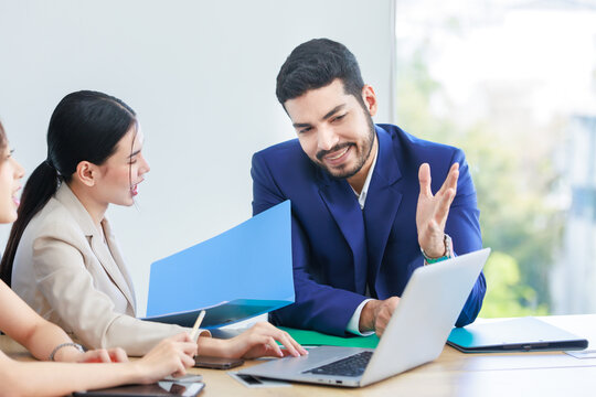 Asian Indian multinational professional successful bearded male businessman explaining discussing brainstorming with female businesswomen colleagues in formal business suit in office meeting room