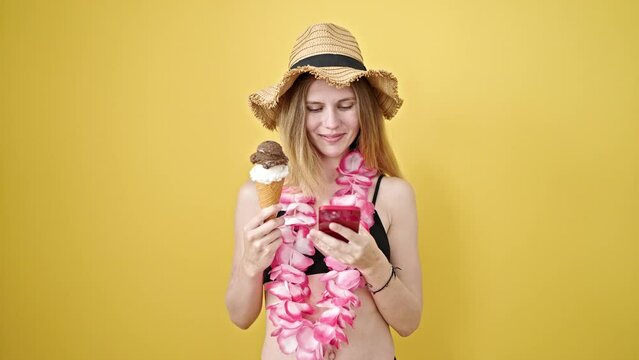 Young blonde woman tourist holding ice cream make selfie by smartphone over isolated yellow background