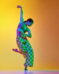 Full-length image of young artistic, expressive woman in stylish costume dancing against gradient yellow orange background in neon light. Concept of modern dance style, hobby, art, lifestyle, ad