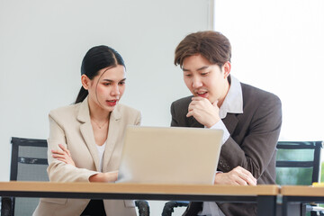 Asian professional successful male businessman explaining discussing brainstorming with female businesswoman colleague in formal business suit via laptop notebook computer in office company workplace