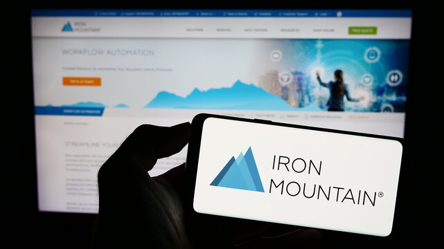 Stuttgart, Germany - 07-29-2023: Person holding cellphone with logo of US company Iron Mountain Inc. on screen in front of business webpage. Focus on phone display.