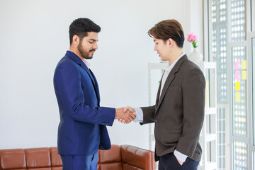 Millennial Asian Indian multinational professional successful businessmen  in formal suit standing shaking hands greeting say hello together in conference meeting room with businesswomen colleagues