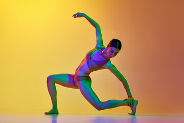 Artistic, talented young woman in underwear dancing contemp against gradient yellow orange background in neon light. Concept of modern dance style, hobby, art, performance, lifestyle, ad