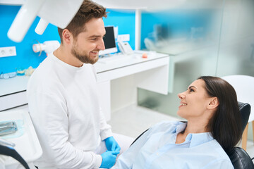 Man dental hygienist consulting woman patient before examination in orthodontic chair