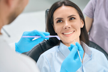 Male dental techician using special medical tools to check female patient teeth and gums health