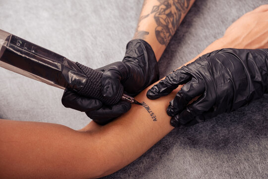 Hands of tattoo artist tattooing word AESTHETIC on client forearm