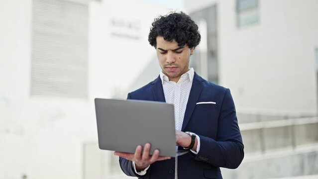 Young latin man business worker using laptop looking clock at street