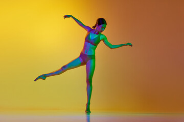 Fototapeta na wymiar Full-length image of young woman, professional dancer in motion, dancing in underwear against gradient yellow orange background in neon light. Concept of modern dance style, hobby, art, lifestyle, ad