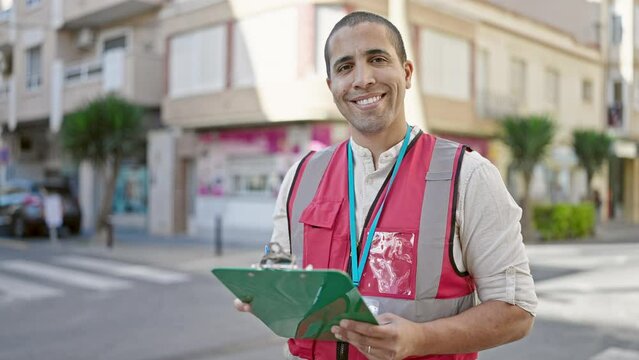 Young hispanic man volunteer smiling holding clipboard at street