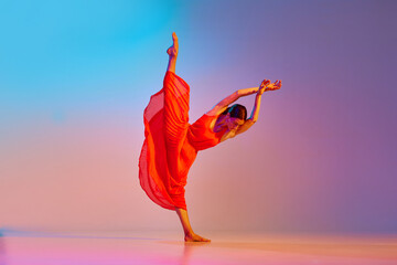 Dynamic image of young talented, artist woman in elegant red dress dancing against gradient...