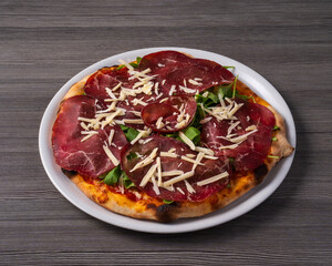 Pizza with bresaola, rocket and parmesan cheese on gray wooden table.
