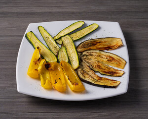 plate of grilled vegetables, peppers, courgettes and aubergines on gray wooden table.