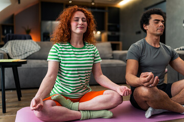 An interracial couple meditates together in the living room, they are dressed casually and like to reset their mindset once a week