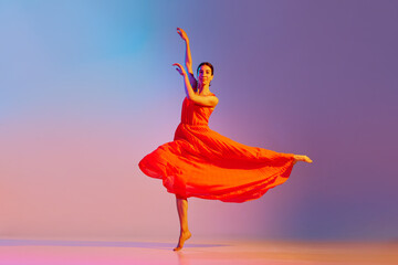 Talented, beautiful young woman in elegant red dress dancing against gradient multicolored...