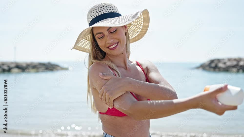 Sticker Young blonde woman tourist wearing bikini applying sunscreen lotion at beach