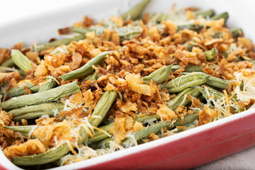 A traditional green bean casserole topped with French Fried Onions and cream of mushroom on white marble. Close up