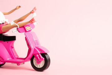 Fototapeta na wymiar The doll's legs are thrown over the handlebars of a pink vintage scooter on a pastel pink background.