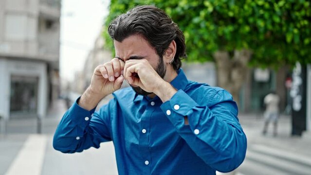 Young hispanic man rubbing the eyes at street