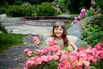 little beautiful girl in a fairy costume of butterfly with wings in princess dress having fun in roses garden on sunny summer day	