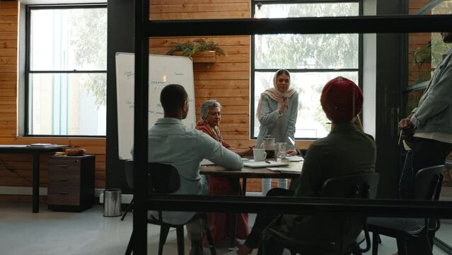 Woman in a hijab discussing an upcoming project with her colleagues in an office meeting. Young business woman speaking with confidence as she shares her ideas and solutions with her team.