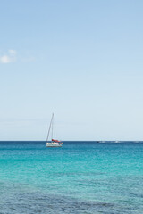 Fototapeta premium Seascape. Turquoise blue sea with sailboat in the background, sky with white clouds. Fuerteventura, Canary Islands, Spain 