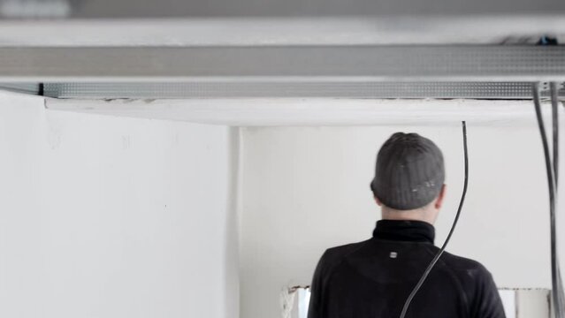 Construction worker assemble a suspended ceiling with drywall and fixing the drywall to the ceiling metal frame with screwdriver. Renovation, construction and do it yourself DIY concept.
