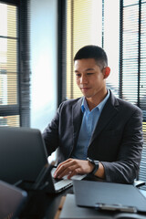 Elegant businessman looking at laptop screen, reading financial report online and writing important notes.