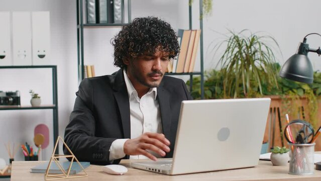 Irritated tired indian business man while working on laptop, unexpected online website problem, computer virus data loss by hacking. Freelancer feeling mad about broken notebook at office workplace