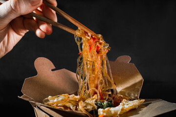 Man eating Chinese instant noodles from a takeaway box with chopsticks