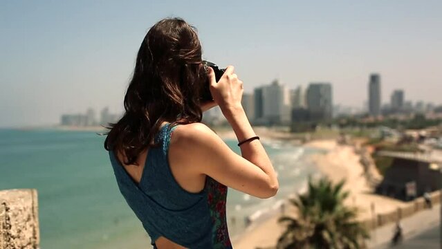 A young and pretty photographer taking a photo with her DSLR camera overlooking a beautiful sandy beach on a hot summers day in america.