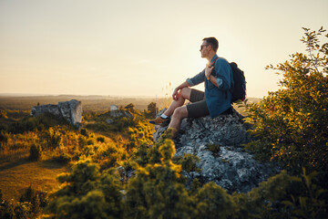 Travel and hiking concept. Adult man with backpack sitting on the edge of rock enjoying landscape...