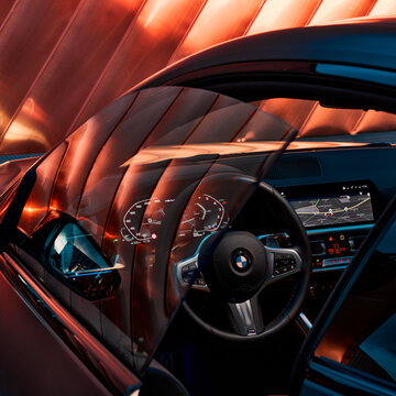 The interior of the BMW 4 at night, seen through the driver's door ajar. In the background, golden panels, illuminated by car headlights, which are reflected in the glass. Zory, Poland, 19.02.2023