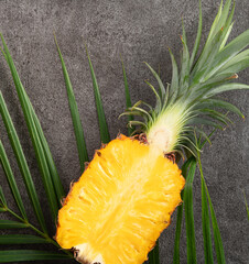 Fresh cut pineapple with tropical leaves on gray table background.