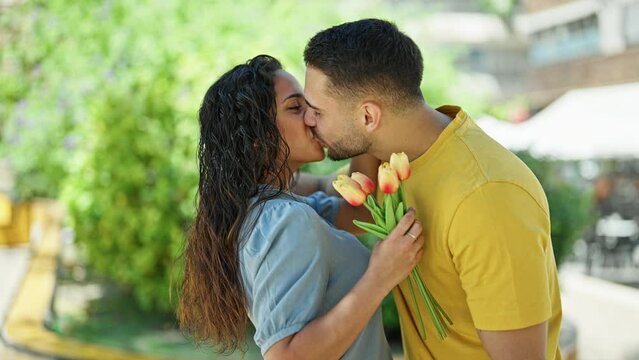 Man and woman couple surprise with bouquet of flowers kissing at park