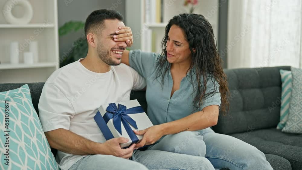 Wall mural Man and woman couple surprised with gift sitting on sofa at home