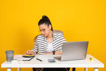 Using calculator, serious business woman sit at office desk with laptop using calculator. Isolated yellow studio background. Working on documents, budget, payment, tax. Young entrepreneur  career.
