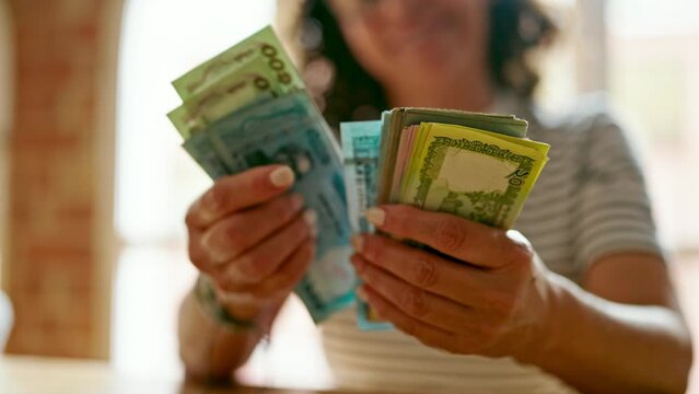Middle age hispanic woman counting bangladesh taka banknotes at home