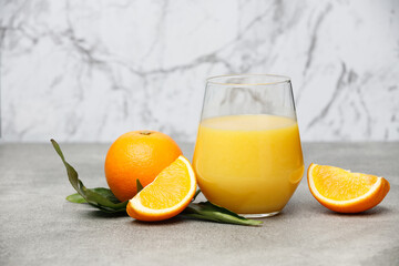 Glass of orange juice and orange slices with leaves on stone table