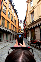 A street in downtown Stockholm, Sweden with the steeple of St. Nicholas Church in the background. Photographed through a cell phone camera of a tourist