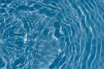 Blue water with ripples on the surface. Defocus blurred transparent blue colored clear calm water surface texture with splashes and bubbles. Water waves with shining pattern texture background.