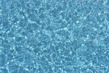 Blue water with ripples on the surface. Defocus blurred transparent blue colored clear calm water surface texture with splashes and bubbles. Water waves with shining pattern texture background.