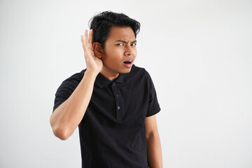 young Asian man looking camera and doing can not hear gesture, trying to listening a gossip wearing black polo t shirt isolated on white background - obrazy, fototapety, plakaty