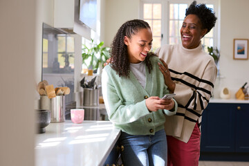 Mother Talking With Teenage Daughter At Home Looking At Social Media On Mobile Phone Together