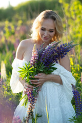 beautiful blond woman in white dress on lupin field summer background close up dawn portrait. High...