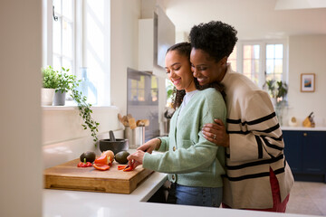 Mother With Teenage Daughter Helping To Prepare Meal At Home In Kitchen Together
