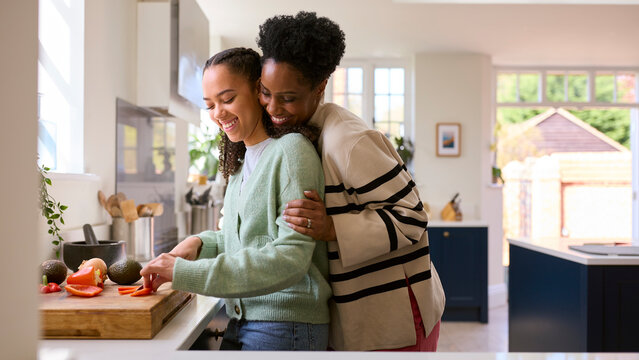 Mother With Teenage Daughter Helping To Prepare Meal At Home In Kitchen Together - Powered by Adobe