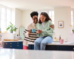 Mother Talking With Teenage Daughter At Home As She Checks Social Media On Mobile Phone